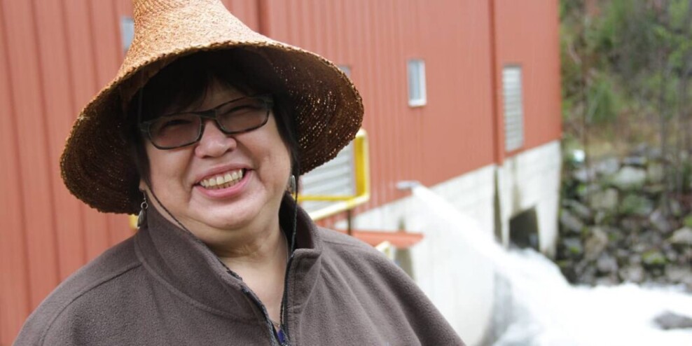 Dr. Judith Sayers, also known as Kekinusuqs, wearing a woven cedar hat and smiling.