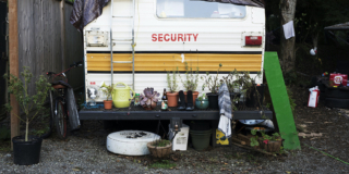 The back end of a camper van. It has plants in pots on the bumper. It looks like someone has lived here for a while.
