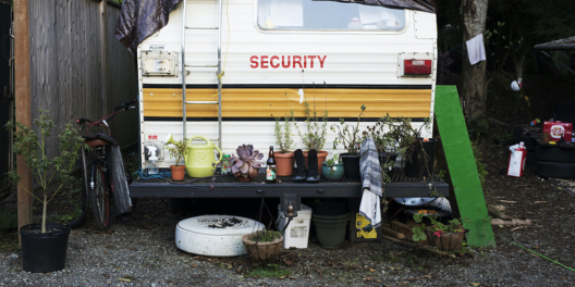 The back end of a camper van. It has plants in pots on the bumper. It looks like someone has lived here for a while.