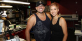 Bill and Natasha Dennis with huge smiles in front of the equipment in their t-shirt printing shop.