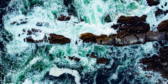 A shot from above of crystal blue waves wrapping around black rocks off the coast of Ucluelet.