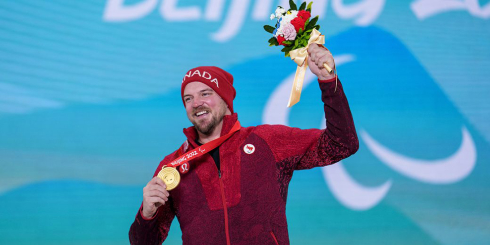 Tyler Turner raises a bouquet of flowers and holds up his gold medal. He has a huge smile on his face.