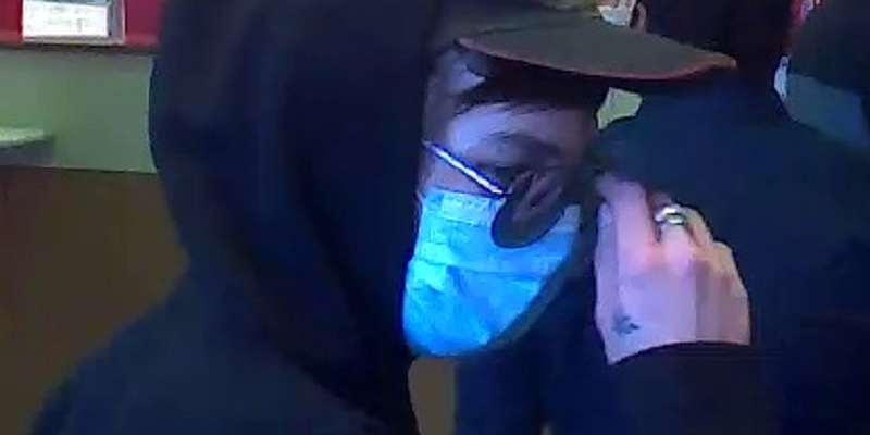 A closeup of a man with a hood, mask, and sunglasses taken from a security camera.